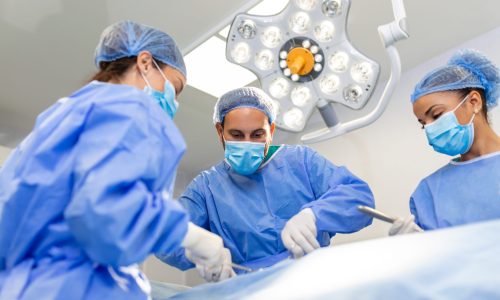 Surgeons doing surgery in operating theatre. Male and female surgeons operating patient. Medical professionals are wearing scrubs.